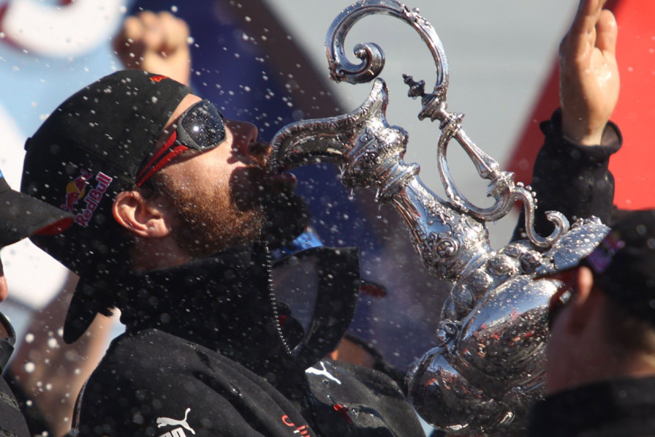 An Oracle Team USA member drinks from the America's Cup trophy. Photo: AFP