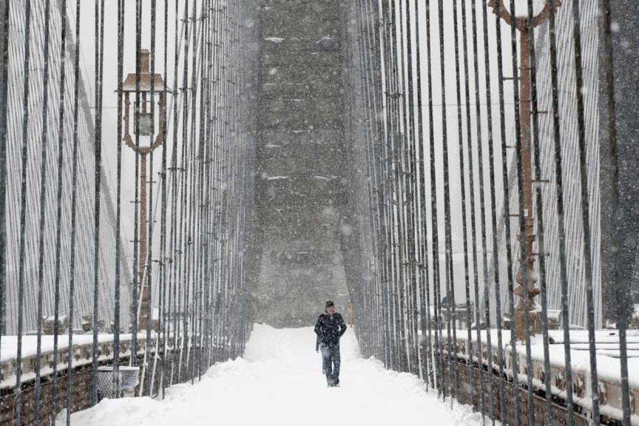 A man crosses Brooklyn Bridge in a snow storm. New Yorkers are great walkers.