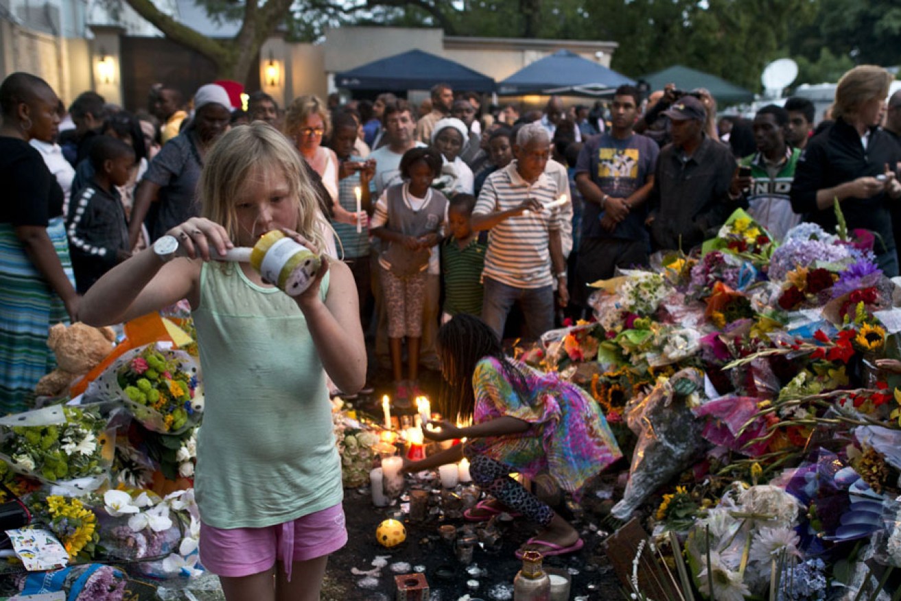 A girl lights a candle for South African former president Nelson Mandela at a wall of flowers laid by mourners outside Mandela's home in Houghton, Johannesburg.