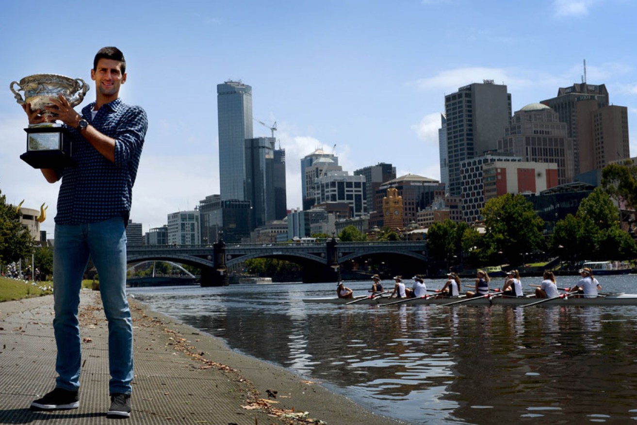 Newly crowned Australian Open champion Novak Djokovic holds the trophy by the Yarra River.