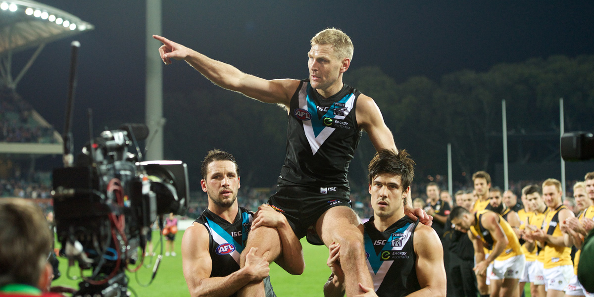 Kane Cornes is carried from the field by captain Travis Boak (left) and Angus Monfries. Photo: Michael Errey/InDaily