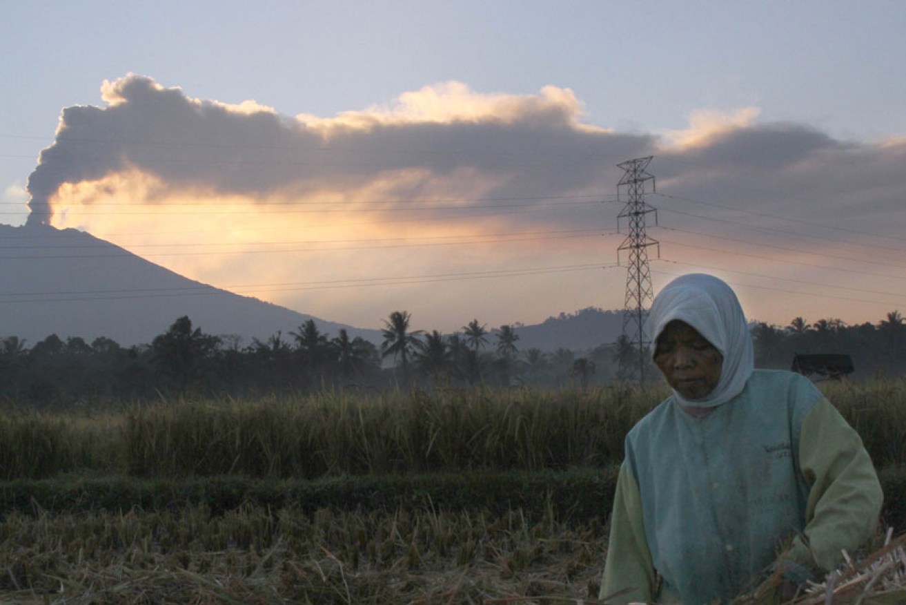 An Indonesian farmer at work while the Mount Raung volcano emits a column of ash and steam.