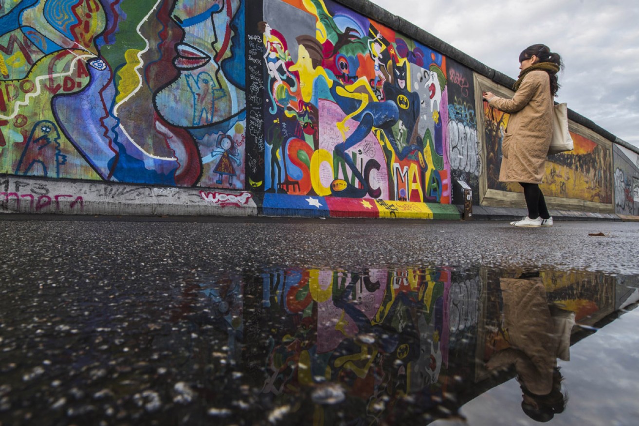 A tourist photographs art on the Berlin Wall. Berlin is considered a 'post-tourism' hot spot.