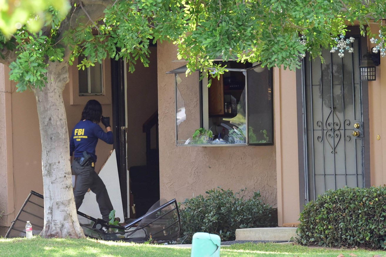 An member of an FBI evidence response team walks over a destroyed door to enter a townhome in Redlands linked to the shooting rampage in San Bernardino. AFP PHOTO /ROBYN BECK