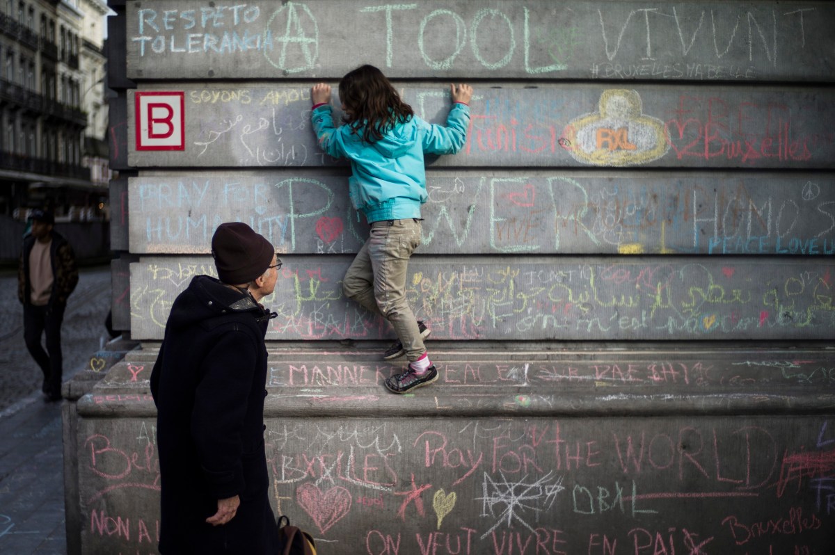 A little girl writes tribute messages on the wall at Place de la Bourse, Brussels. Photo: EPA/Yoan Valat