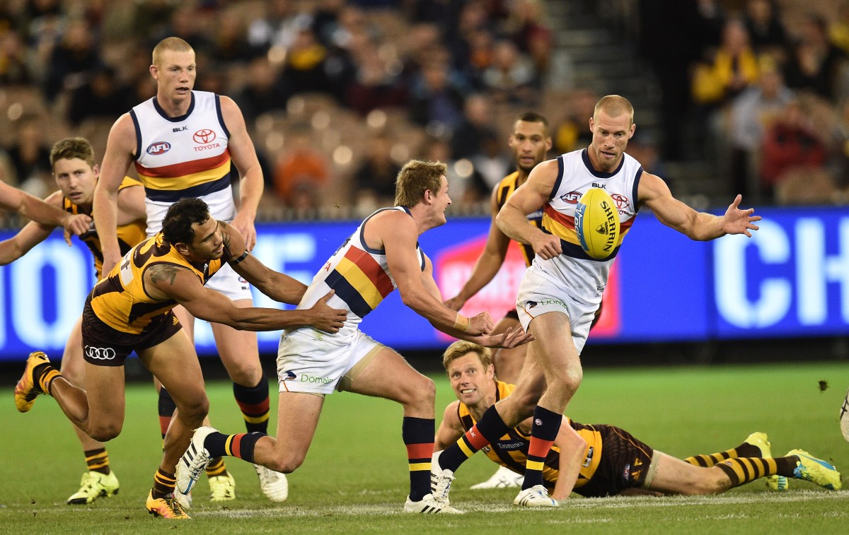 Matt Crouch (second from left) of the Crows handballs to teammate Scott Thompson (right) as of Cyril Rioli (left) the Hawks tackles during the round 5 AFL match between the Hawthorn Hawks and Adelaide Crows at the MCG in Melbourne, Friday, April 22, 2016. (AAP Image/Julian Smith) NO ARCHIVING, EDITORIAL USE ONLY