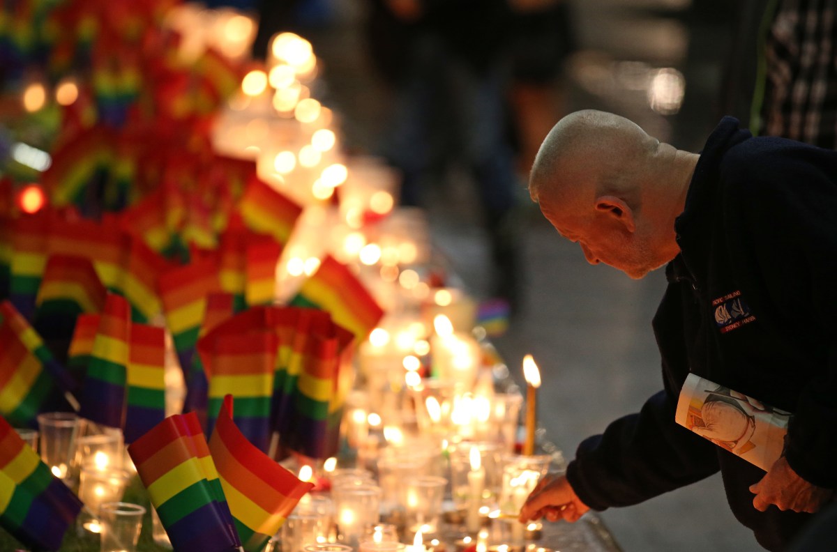 A man places a candle at an impromptu memorial set up in Sydney, Monday, June 13, 2016, following the Florida mass shooting at the Pulse Orlando nightclub where police say a gunman wielding an assault-type rifle opened fire, killing at least 50 people and wounding dozens. Australian Prime Minister Malcolm Turnbull said that the Orlando mass shooting was "an attack on all of us — on all our freedoms, the freedom to gather together, to celebrate, to share time with friends." (AP Photo/Rick Rycroft)