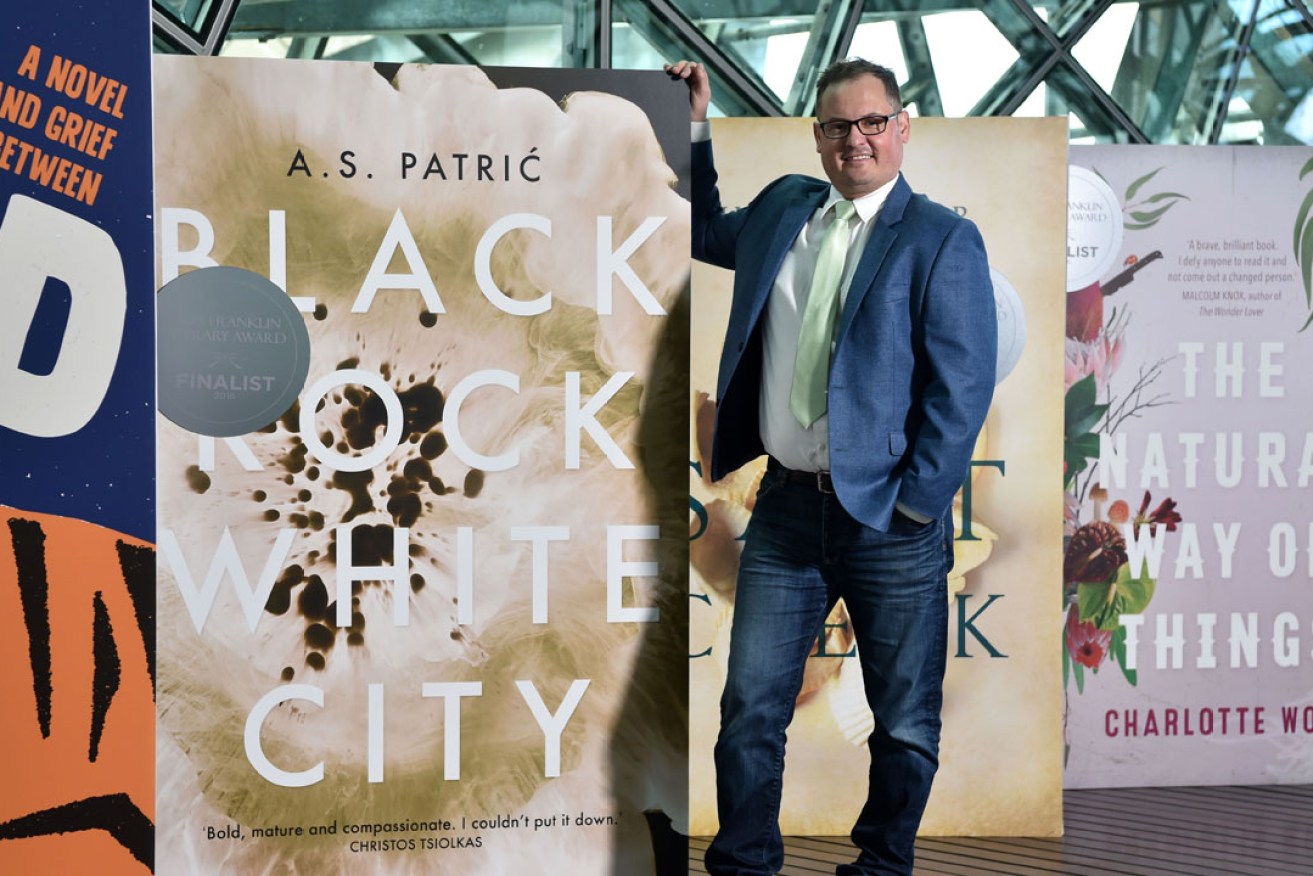 Alec Patric with a large image of the cover of his book alongside those of previous Mile Franklin Literary Award winners. Photo: supplied
