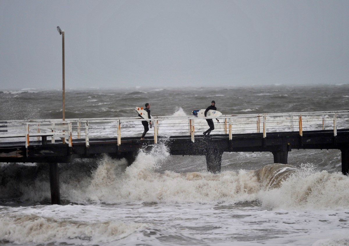 Surfers on a jetty look to jump into the waves that have been created by a storm front on Adelaide metropolitan beaches. Photo: AAP/David Mariuz