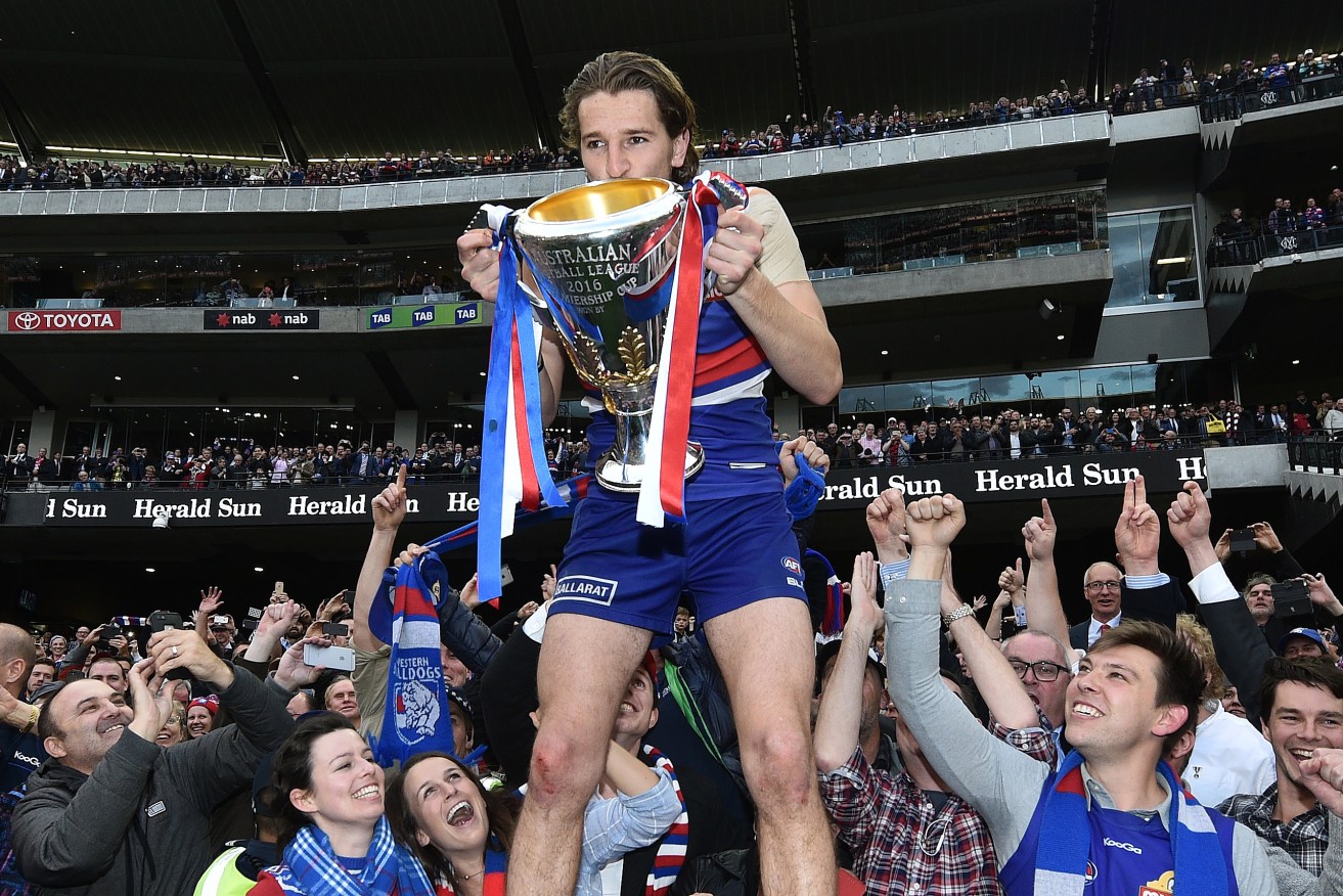 Marcus Bontempelli holds the premiership cup, flanked by Bulldogs supporters. Photo: Julian Smith / AAP