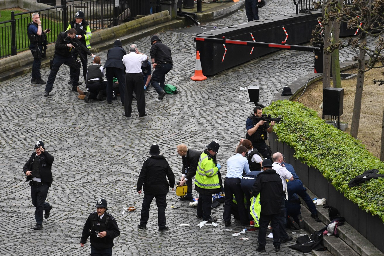 A policeman points a gun at a man on the ground (top of the frame) as emergency services attend the scene outside the Palace of Westminster, London. Photo: Stefan Rousseau/PA Wire