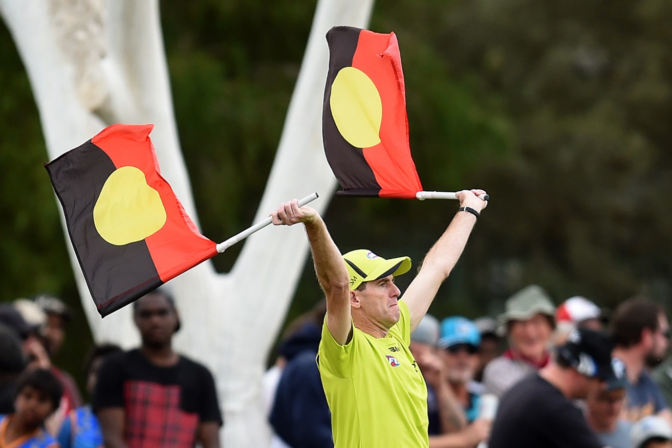 A goal umpire uses Aboriginal flags to signal a goal during Port Adelaide's game against Melbourne in Alice Springs last year. Photo: Dan Peled / AAP
