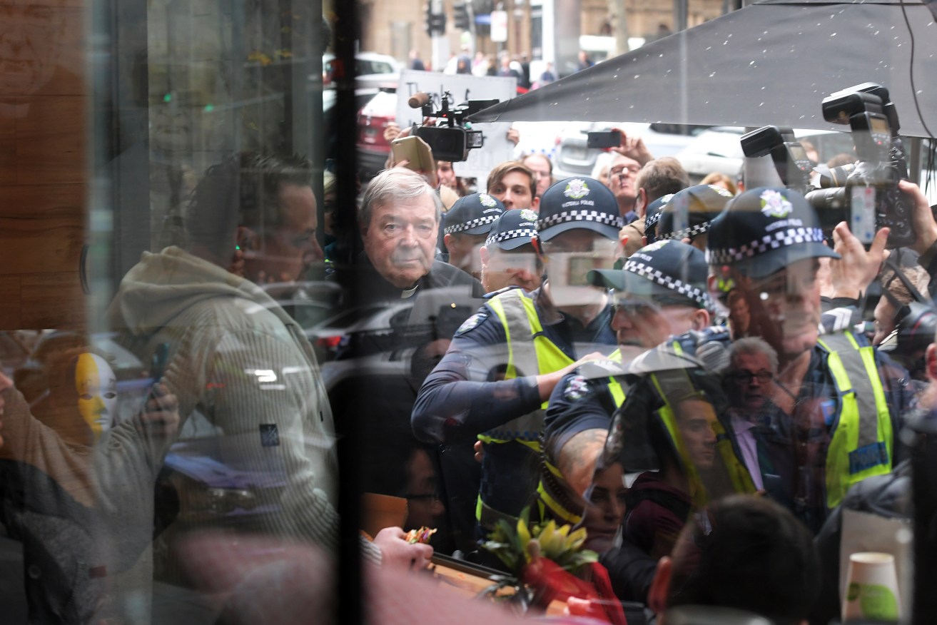 Cardinal George Pell (top and centre, looking directly at camera) leaves the Melbourne Magistrates Court today escorted by police and surrounded by a huge media contingent. Photo: AAP /Tracey Nearmy
