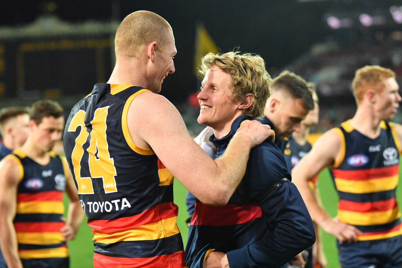 TRIUMPH AND TRAGEDY: Sam Jacobs, who played despite the death of his brother last week, embraces Rory Sloane, who missed the game after appendix surgery, as a despondent Brodie Smith walks behind them. Photo: David Mariuz / AAP