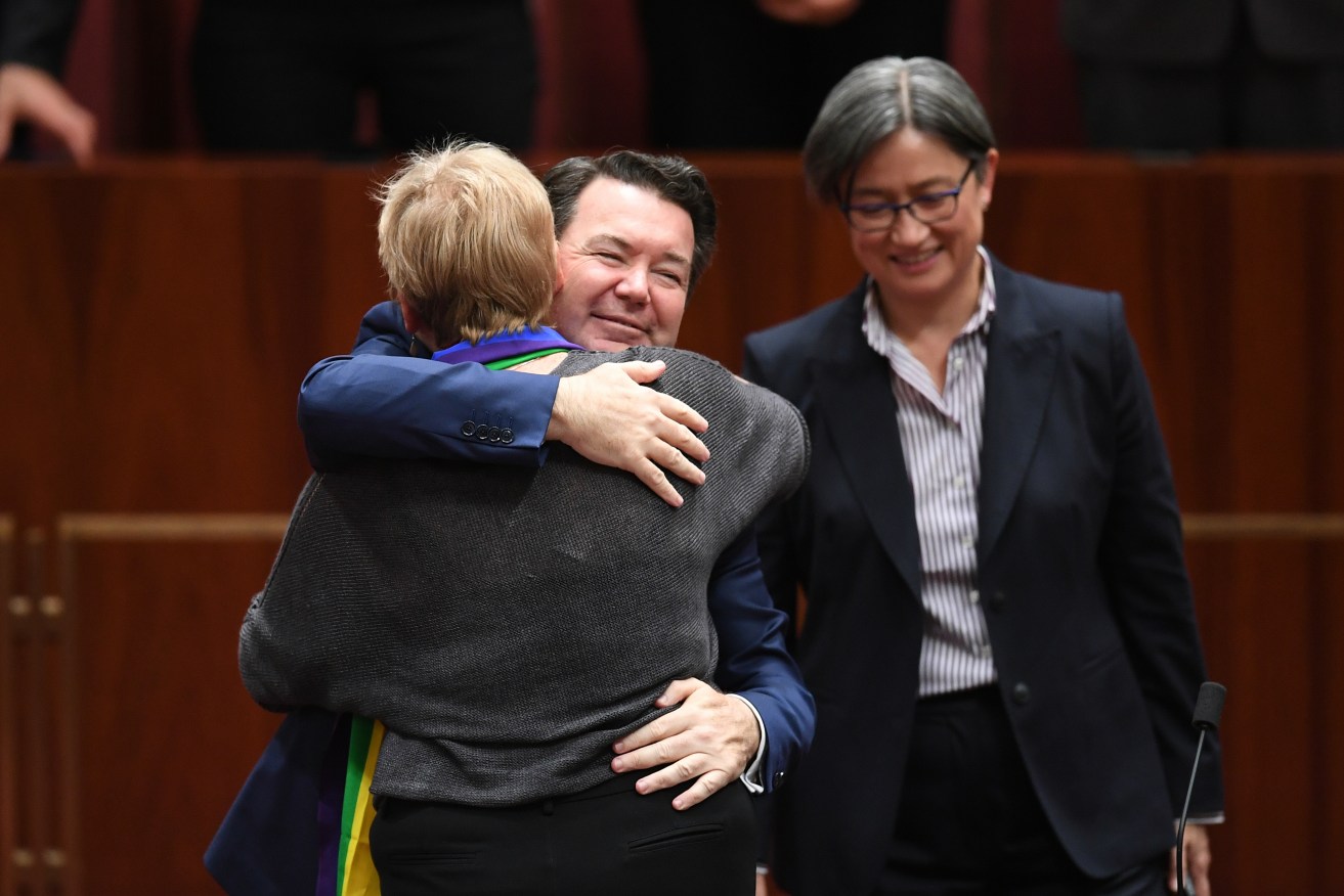 Liberal Senator Dean Smith hugs Australian Greens Senator Janet Rice while Penny Wong (right) looks on. Photo: AAP/Lukas Coch
