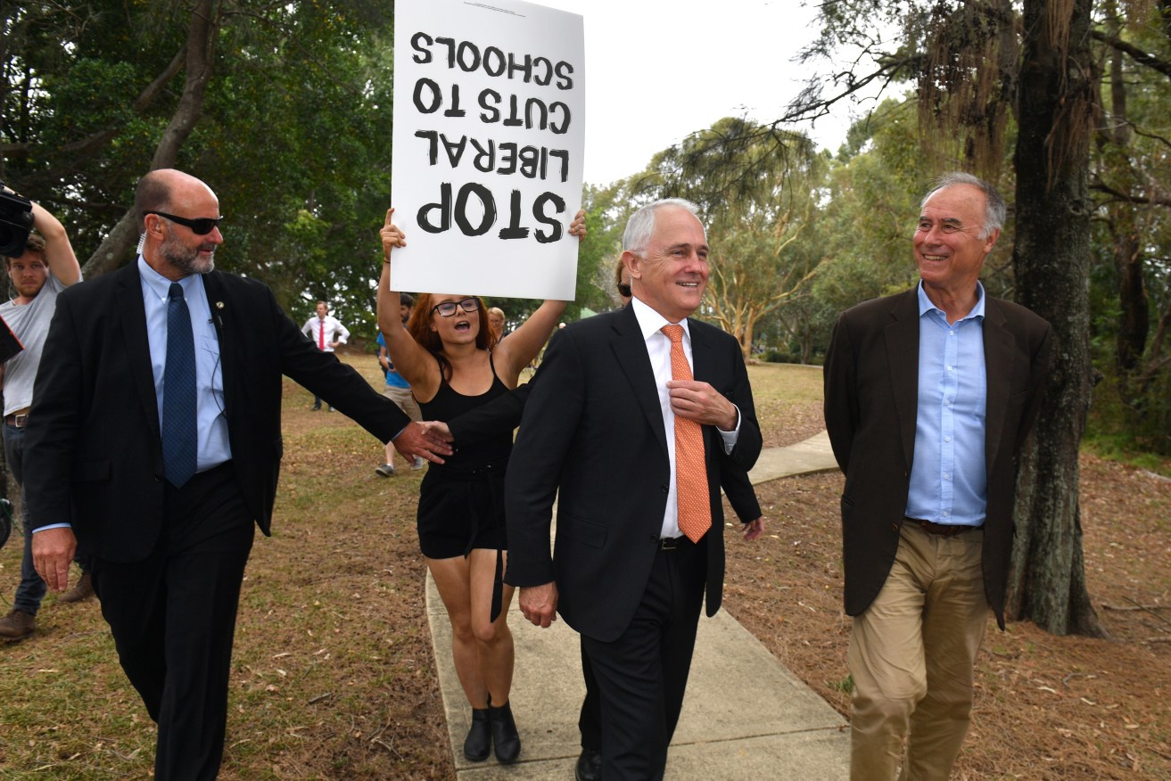A protester doesn't quite get it right as she confronts Prime Minister Malcolm Turnbull and Liberal candidate for Bennelong John Alexander after a press conference in Sydney today. Photo: AAP/Mick Tsikas