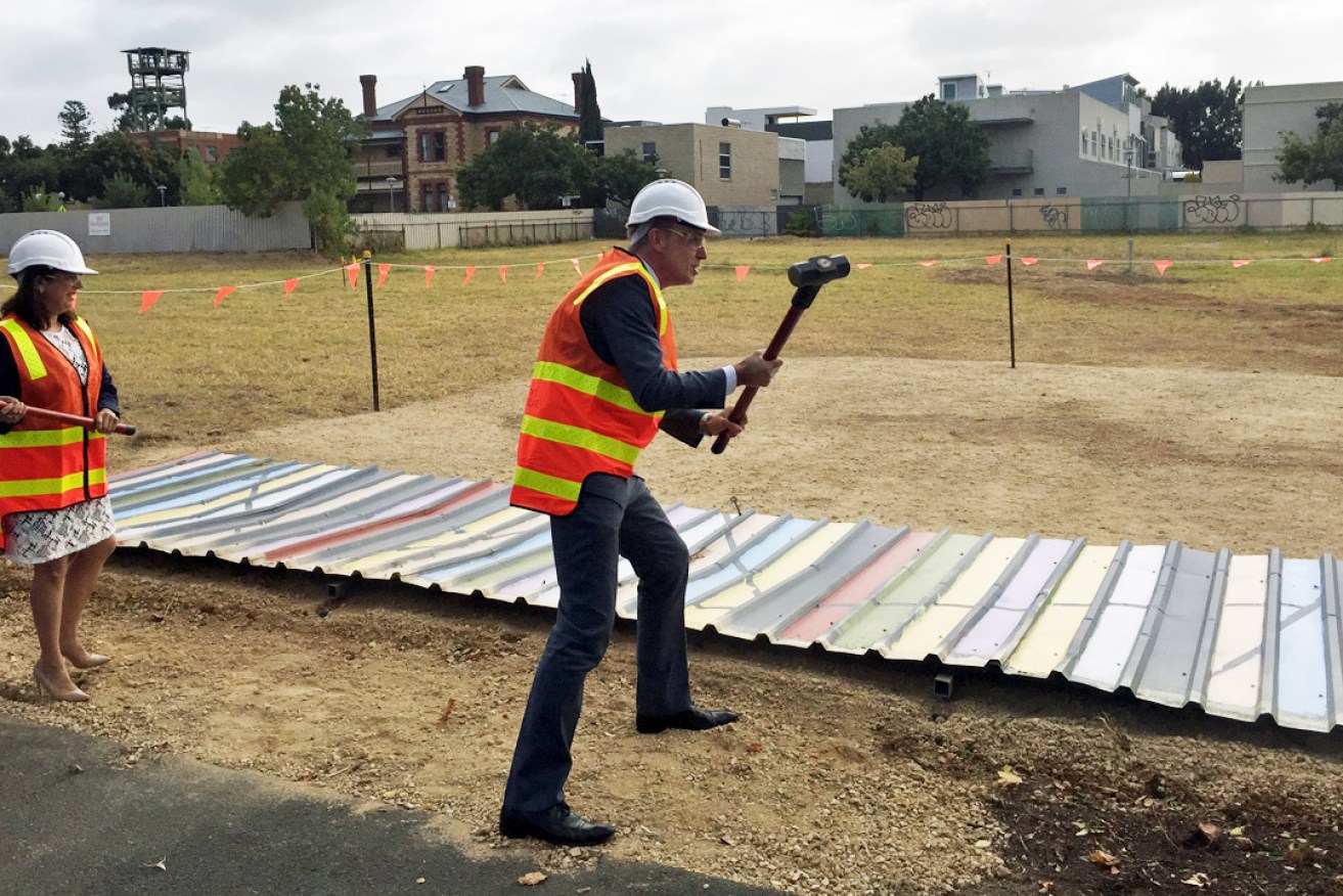 Area councillor Natasha Malani (left) and Lord Mayor Martin Haese theatrically knocking down a pre-prepared section of the old Le Cornu site fence after the council bought the property. Photo: Bension Siebert / InDaily