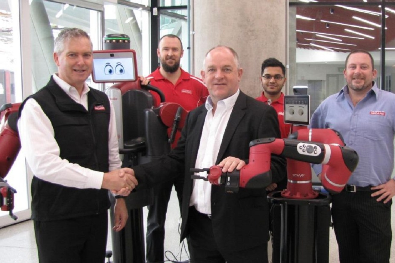 REDARC founder Anthony Kittel, left, shakes hands with the Chair of Information Technology at Flinders, Professor John Roddick, alongside one of the smart robots that his firm co-purchased for use by science and engineering students.
