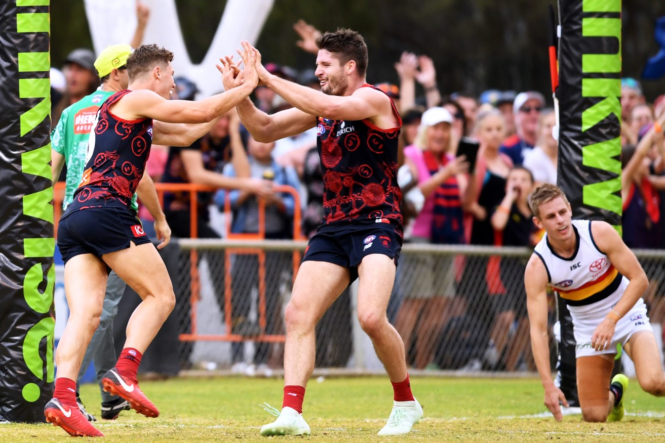 Adelaide's David Mackay looks on as Demons Jake Melksham and Jesse Hogan celebrate another goal. Photo: AAP/Mark Brake