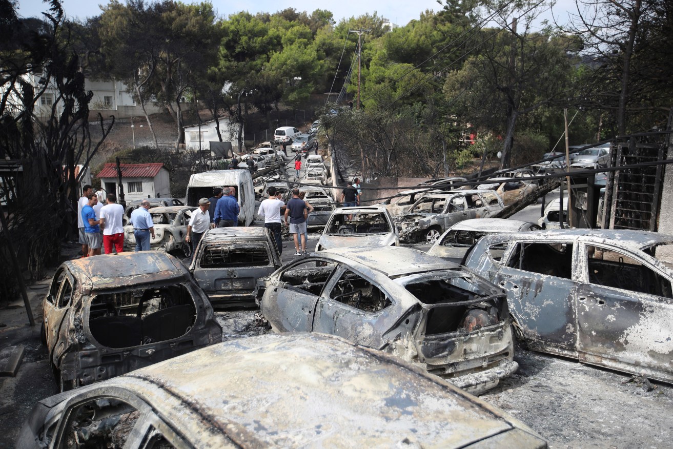 People stand amid the charred remains of burned-out cars in Mati east of Athens. Photo: AP/Thanassis Stavrakis