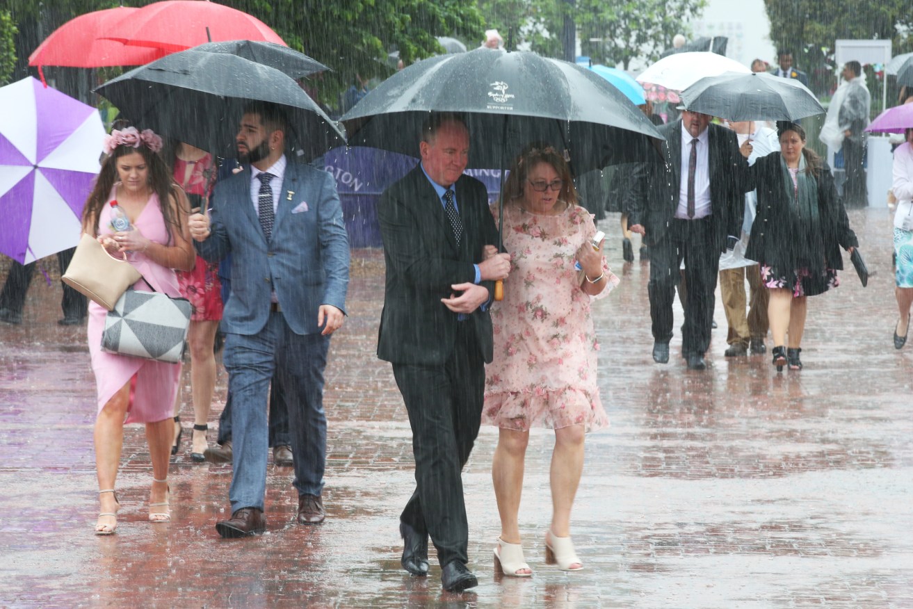 Racegoers get caught in heavy rain at Flemington this morning. Photo: AAP/Dave Crosling