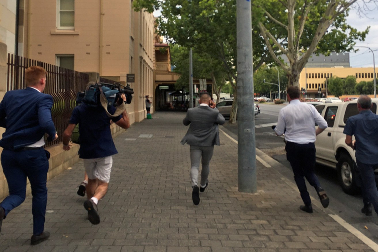Moujtaba Joubouri (centre) was chased by the media, leaving the Adelaide Magistrate's Court this morning. Photo: Bension Siebert / InDaily
