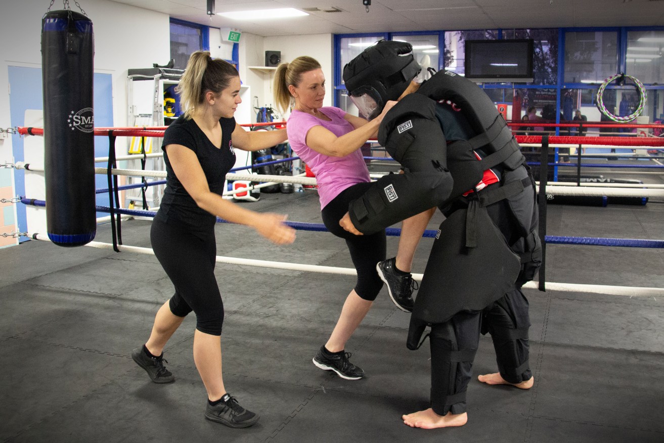 Carly Gangell with a client who is kneeing a self defence instructor wearing a "full contact suit". Photo: James Carroll. 