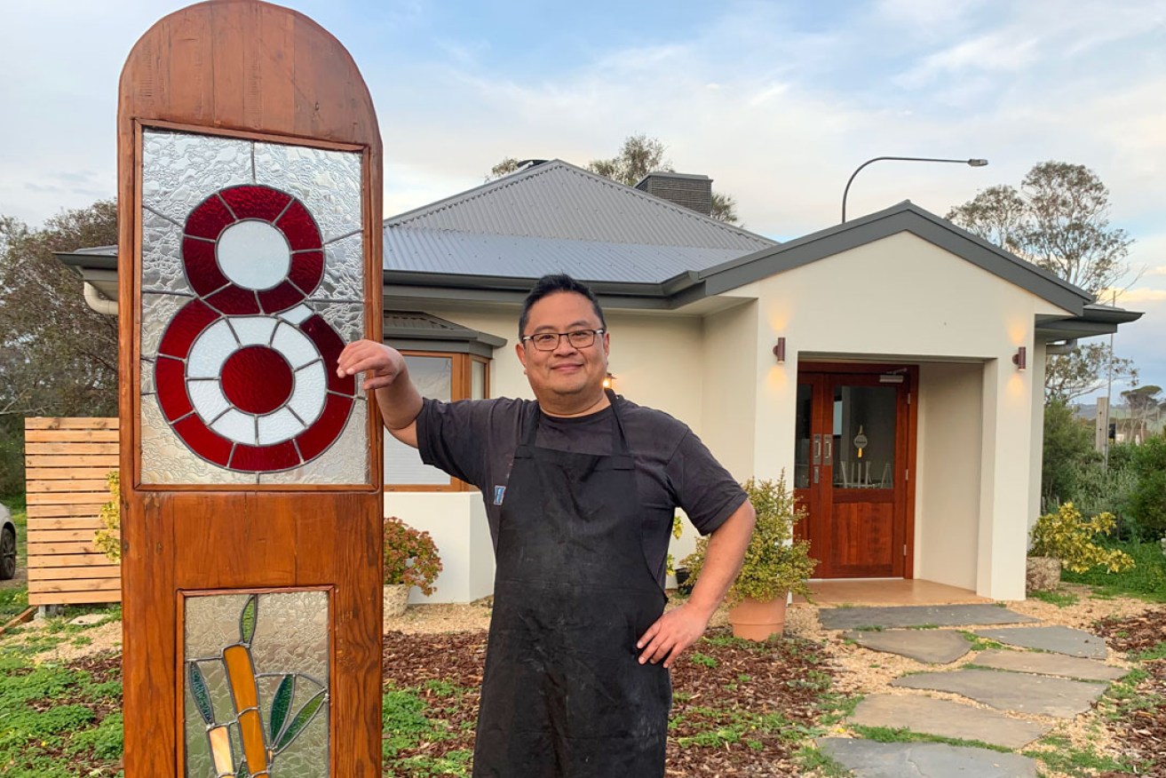 Francis Tan alongside the Lot 8 sign, crafted by an Aldinga Arts EcoVillage resident.