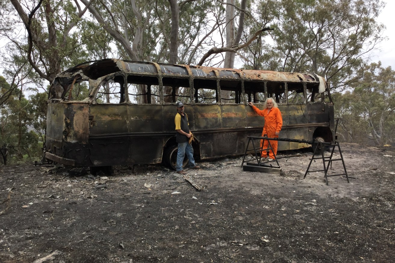 Daniel Kelly (right) and Mathew Fowler next to Kelly's burnt out heritage bus on his property at Lobethal. Photo: AAP/Kathryn Bermingham