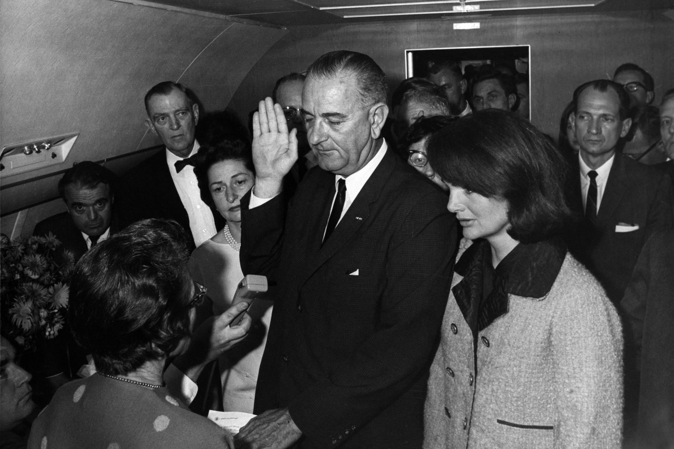 Lyndon B. Johnson taking the oath of office aboard Air Force One  two hours and eight minutes after the assassination of John F. Kennedy, Dallas, Texas. Jackie Kennedy (right), still in her blood-soaked clothes, looks on. 