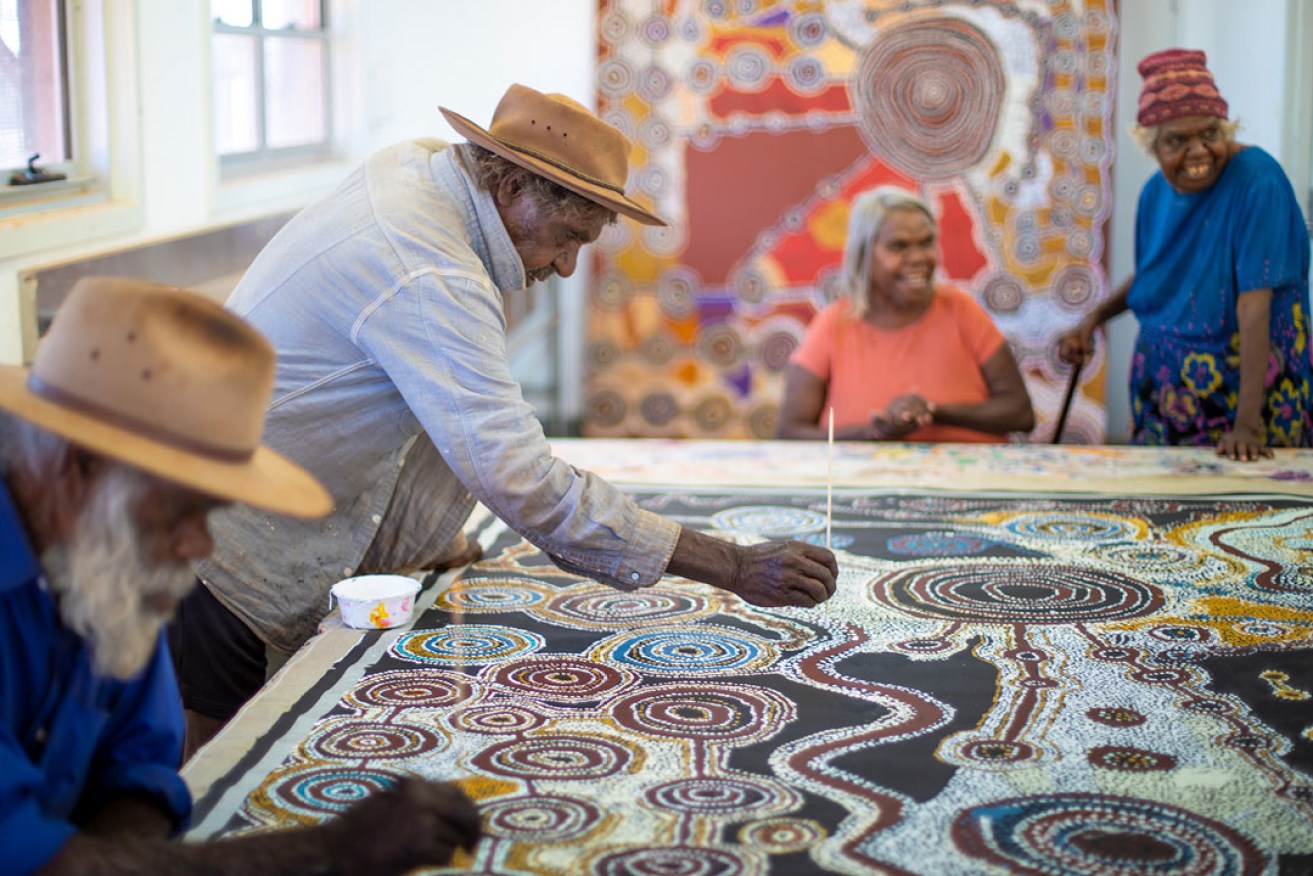 Taylor Cooper and Witjiti George working on a collaborative painting under the watchful eye of Matjangka Norris and Tjangali George; courtesy the artists and Kaltjiti Arts. Photo: Meg Hansen 