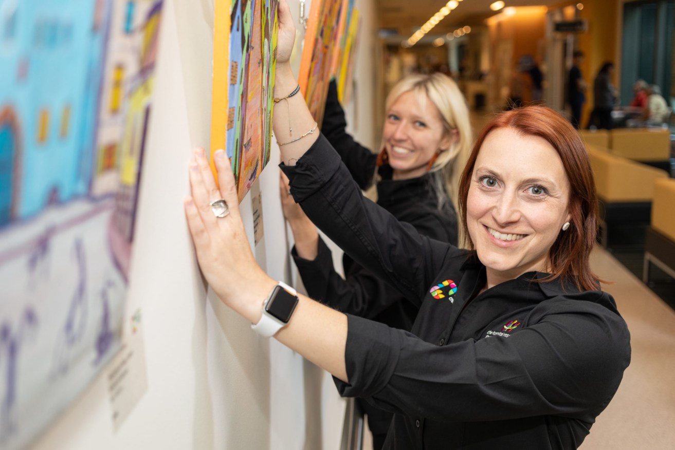 Centre for Creative Health senior curator Fiona Borthwick and assistant curator Steph Cibich install "Small Stories of Great Cities" by Irina Mirosnitsenko at the Royal Adelaide Hospital. Photo supplied by CCH