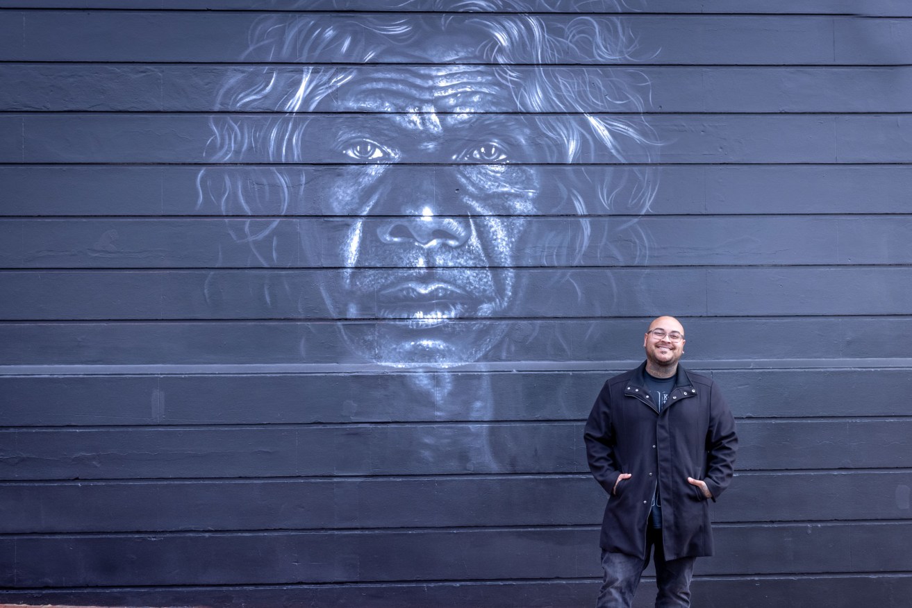 Artist Thomas Readett with his mural of David Gulpilil on the wall of Tandanya National Aboriginal Cultural Institute on East Terrace. Photo: Razan Fakhoury