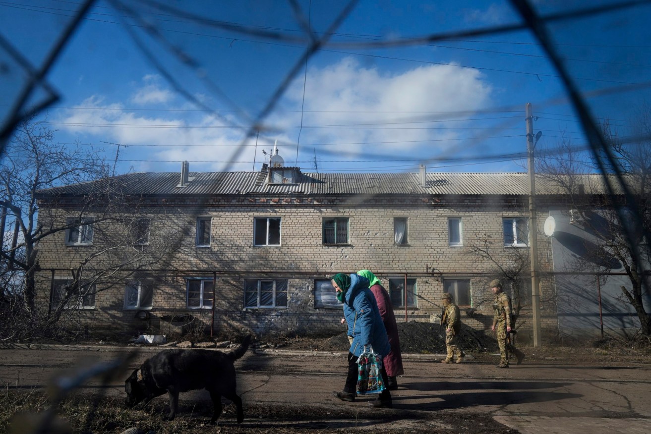 Two Ukrainian soldiers patrol a street as elderly women walk past a house damaged by artillery shelling in Novoluhanske, eastern Ukraine, Wednesday, Feb. 23, 2022. (AP Photo/Evgeniy Maloletka)