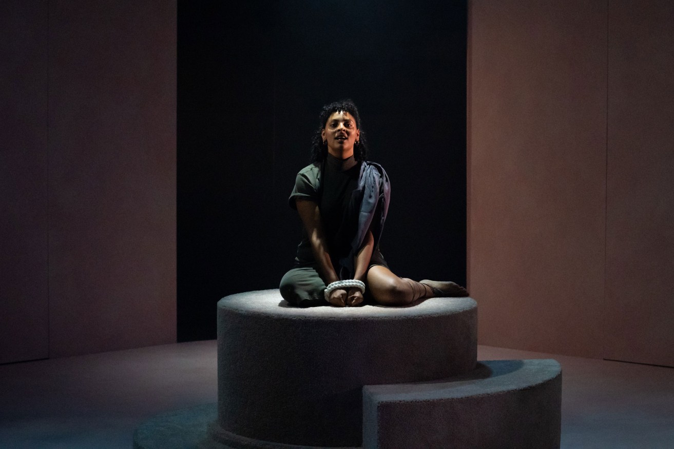 Kidaan Zelleke as Antigone, bound and kneeling on a podium after being caught defying the law and burying her brother. Photo: Matt Byrne