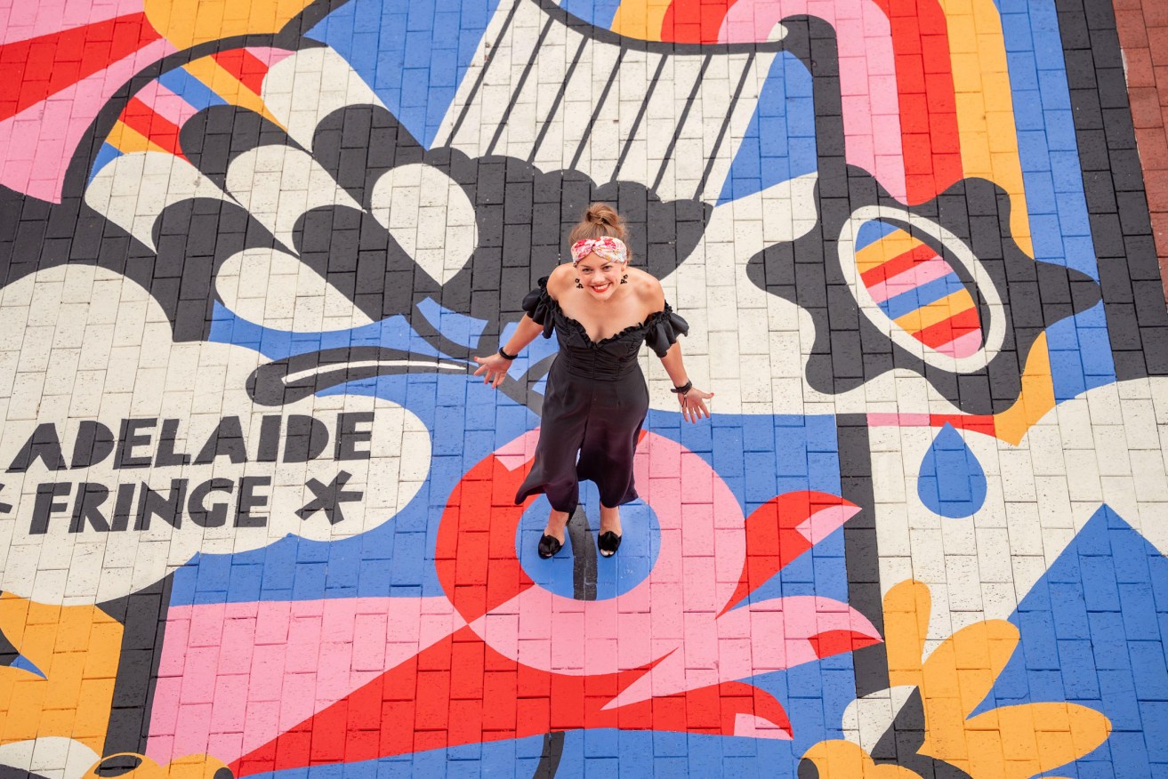 Alana Naylor stands on a mural of her prize-winning 2023 Fringe artwork. Photo: supplied