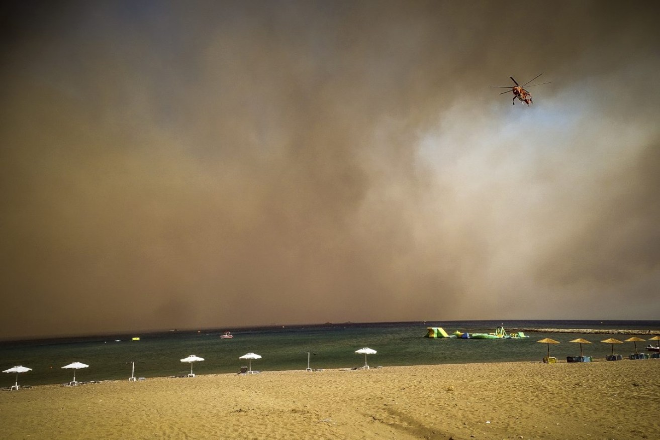 A firefighting helicopter flies over a Rhodes beach. Photo: Argyris Mantikos/Eurokinissi via AP